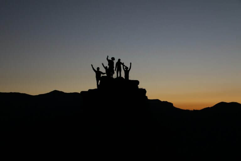 Leadership isn't Given, it's Earned. Group of People at the top of a mountain at sunset