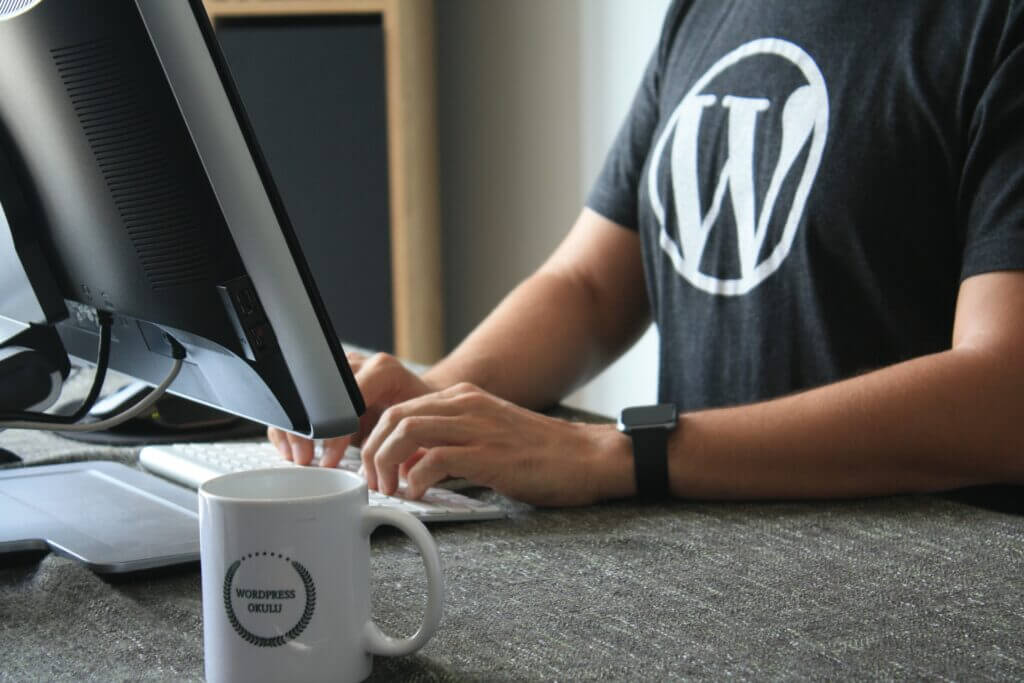 Person wearing black t-shirt with the WordPress "W" logo building a type of WordPress website